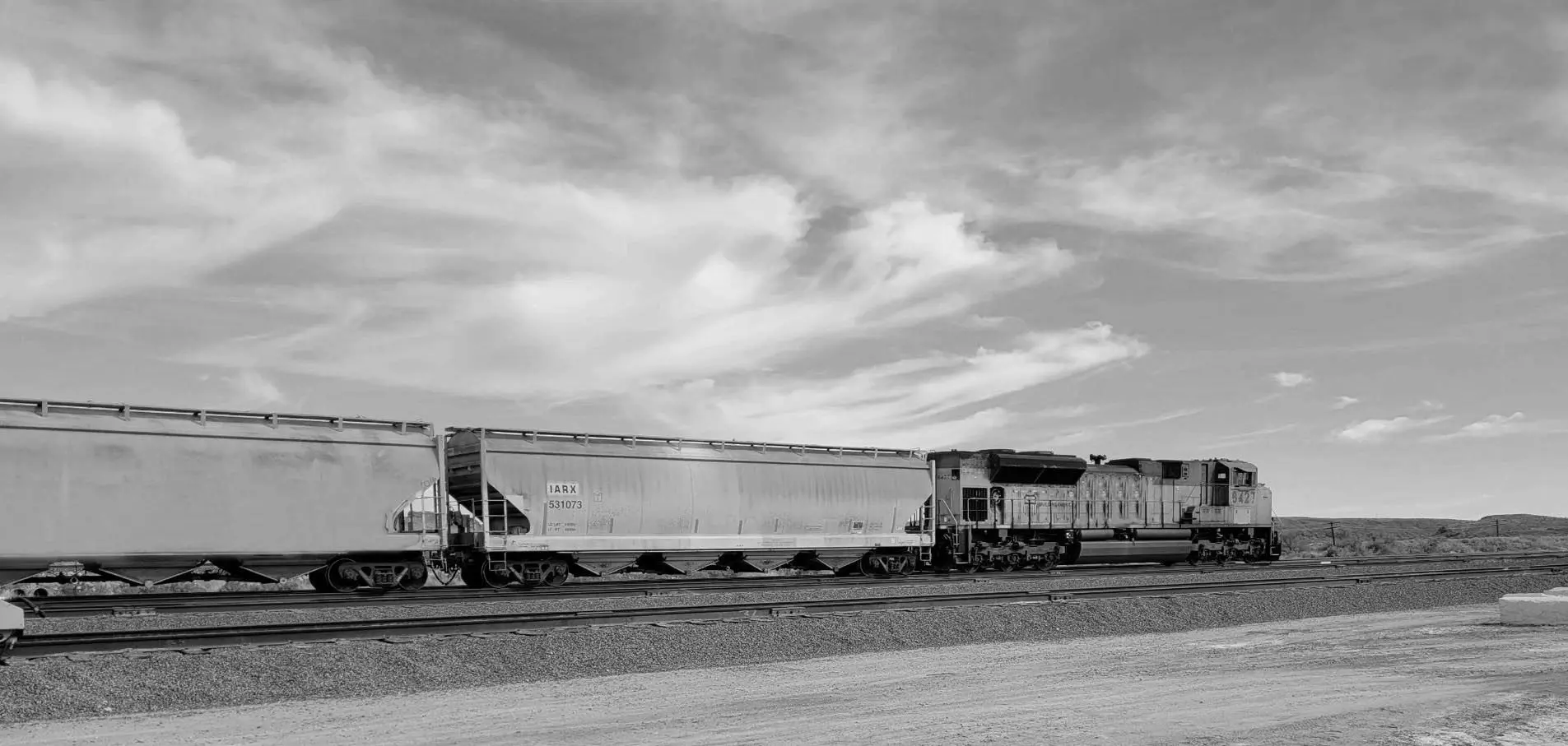 A train is traveling down the tracks in black and white.