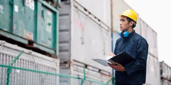 A man in hard hat holding clipboard and looking at camera.